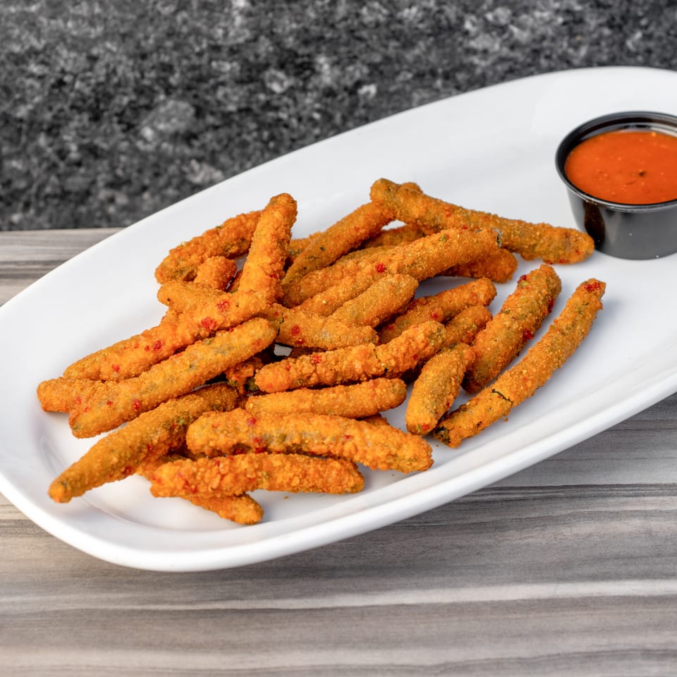 A white platter filled with crispy fried pickle spears and a side of red dipping sauce.