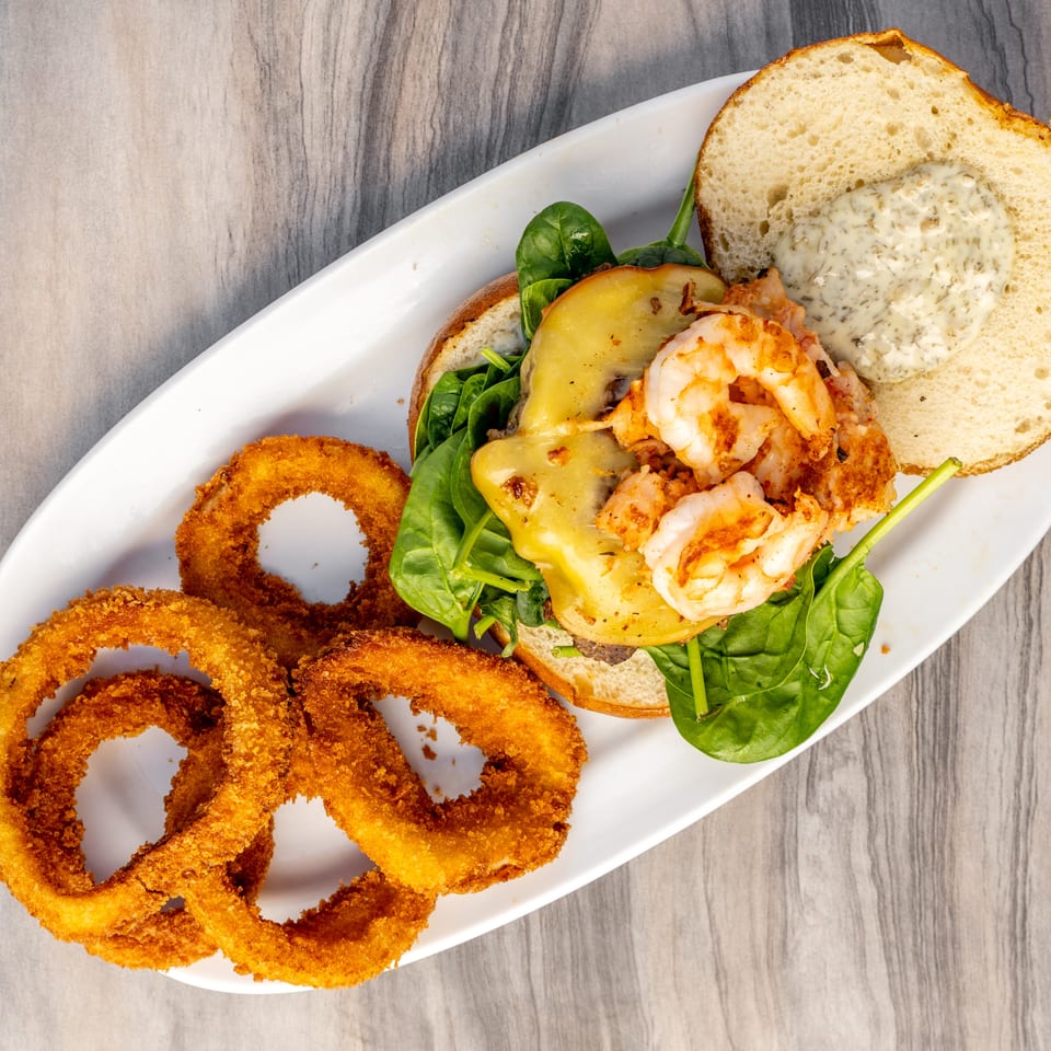 Overhead view of a shrimp burger with melted cheese, spinach, and a side of onion rings.