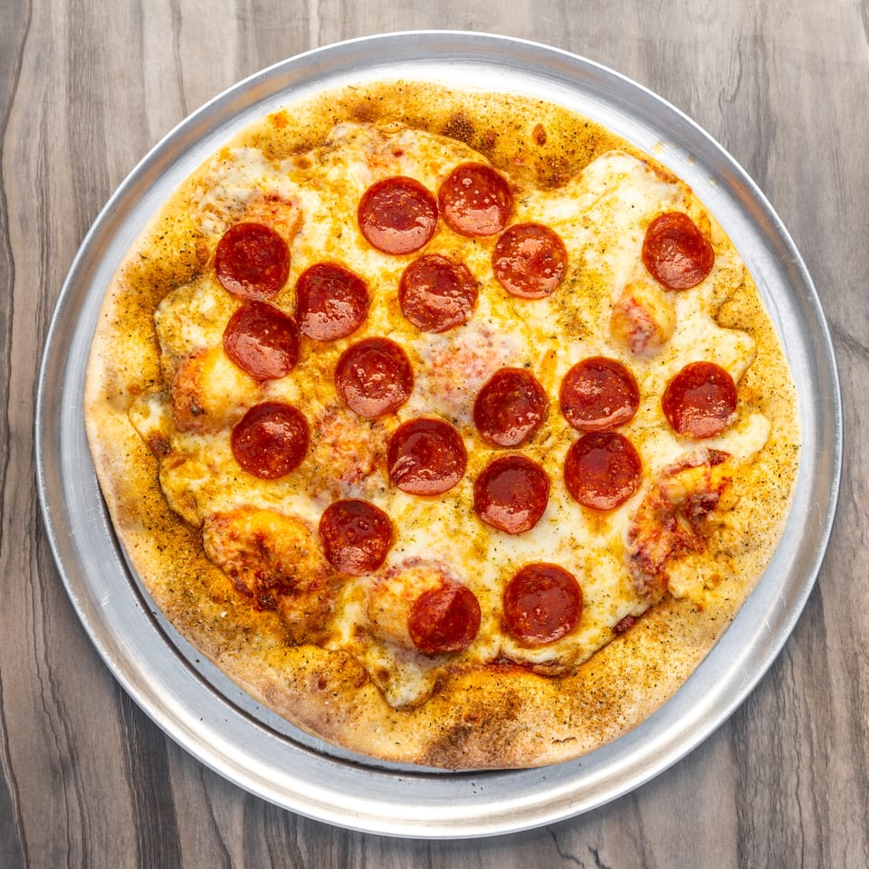 A whole pepperoni pizza with melted cheese on a metal tray, viewed from directly above.