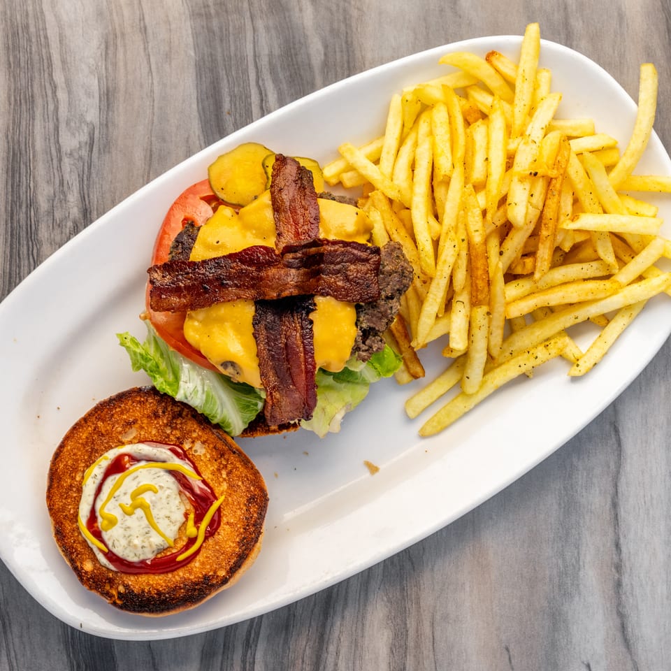 Overhead view of a bacon cheeseburger with lettuce, tomato, pickles, and a side of fries.