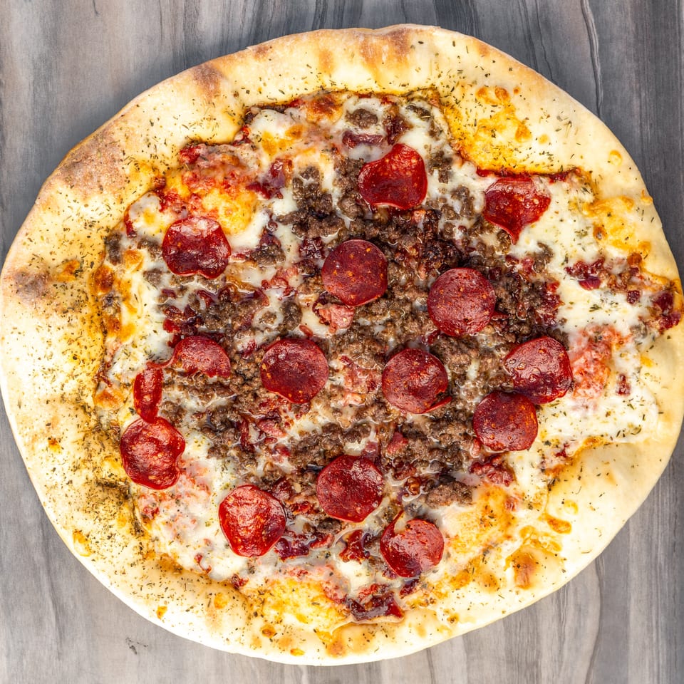 Overhead view of a whole pepperoni and ground beef pizza with melted cheese and herbs.