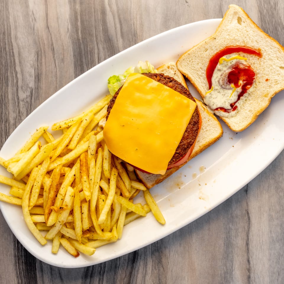 Open-faced burger with cheese, lettuce, tomato, and fries on a white plate.